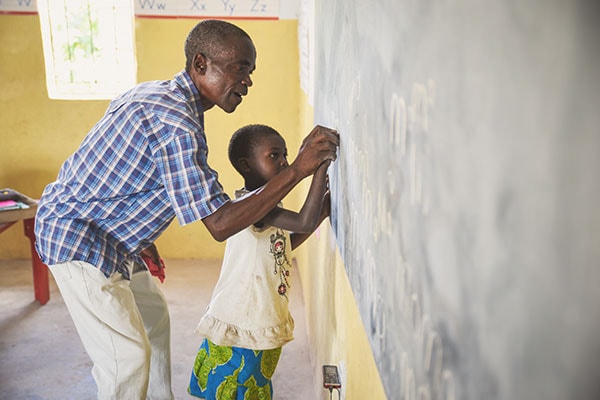 teacher helping student at a chalkboard in a rural school in Zambia